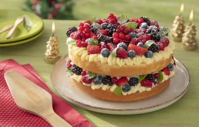 Foto da receita de bolo pelado naked cake natalino sem glúten servida sobre uma base bege em cima de uma mesa verde com decorações de natal, além de um pano vermelho com uma espátula de madeira em cima
