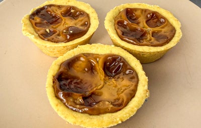 Fotografia em tons claros com várias empadinhas ao centro. Cada empadinha possui uma massa amanteigada e um recheio de leite moça de cor caramelizada