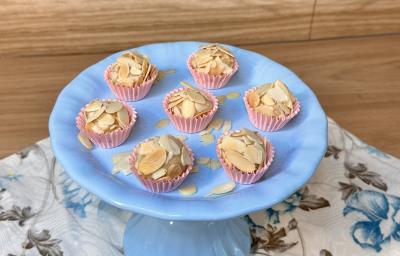 Fotografia em tons de azul e rosa com um prato azul ao centro. Em cima do prato, existe 7 brigadeiros de caramelo salgado cobertos com amêndoas laminadas.