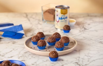 Fotografia mostra brigadeiros enrolados com granulado em forminhas azuis. No fundo, a lata de leite moça. Fotografia mostra brigadeiros enrolados com granulado em forminhas azuis. No fundo, a lata de leite moça.