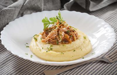 Fotografia em tons de cinza, branco e amarelo, prato branco ao centro com polenta, frango desfiado e salsa, ao lado um garfo base, sobre toalha com listras brancas e cinza e ao fundo guardanapo cinza. Fotografia em tons de cinza, branco e amarelo, prato branco ao centro com polenta, frango desfiado e salsa, ao lado um garfo base, sobre toalha com listras brancas e cinza e ao fundo guardanapo cinza.