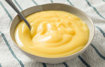 Foto aproximada de um pote redondo com um creme amarelo dentro e uma colher, tudo sobre um tecido de cor bege com listras verdes Foto aproximada de um pote redondo com um creme amarelo dentro e uma colher, tudo sobre um tecido de cor bege com listras verdes