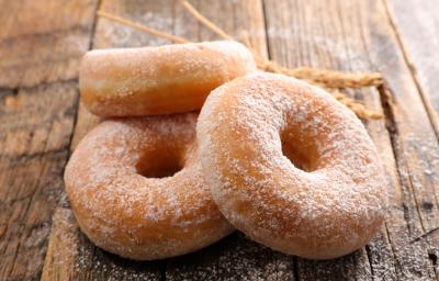 Fotografia de três rosquinhas, uma apoiada na outra, passadas no açúcar de confeiteiro, sobre uma mesa de madeira.