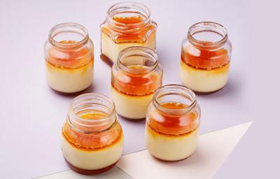 fotografia em tons de branco e laranja vista de cima, contém 6 potinhos transparentes com pudim de dentro e cobertura de caramelo por cima fotografia em tons de branco e laranja vista de cima, contém 6 potinhos transparentes com pudim de dentro e cobertura de caramelo por cima