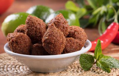 Fotografia em tons de verde com um prato fundo branco ao centro. Dentro do prato existe vários mini kibes feitos na Air fryer. Ao fundo existe limões inteiros e pimentas. Ao lado do prato existe um ramo de hortelã Fotografia em tons de verde com um prato fundo branco ao centro. Dentro do prato existe vários mini kibes feitos na Air fryer. Ao fundo existe limões inteiros e pimentas. Ao lado do prato existe um ramo de hortelã