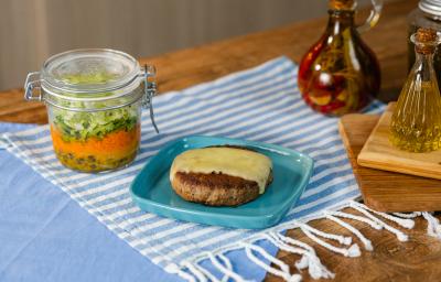Fotografia em tons de azul com um prato azul ao centro. Em cima do prato existe uma receita de hambúrguer no prato acompanhada por uma fatia de queijo muçarela e uma salada no pote feita com alface e cenoura Fotografia em tons de azul com um prato azul ao centro. Em cima do prato existe uma receita de hambúrguer no prato acompanhada por uma fatia de queijo muçarela e uma salada no pote feita com alface e cenoura
