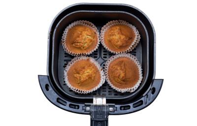 Fotografia vista de cima de quatro muffins de banana sem glúten dentro da cestinha da air fryer, a qual está sobre um fundo branco. Fotografia vista de cima de quatro muffins de banana sem glúten dentro da cestinha da air fryer, a qual está sobre um fundo branco.