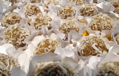 Fotografia de docinhos de beijinho com batata doce, passados no coco ralado e em forminhas de brigadeiro na cor branca, sobre uma mesa amarela.