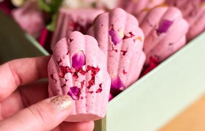 Fotografia em tons de rosa com vários doces cor de rosa ao centro. Esses doces possuem formato de concha e estão dispostos lado a lado.
