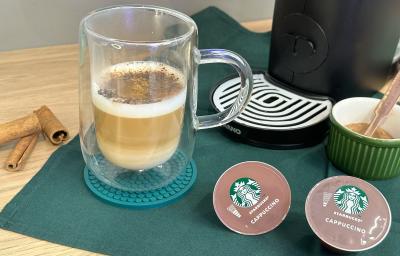 Foto da receita de Cappuccino Canela. Observa-se um copo transparente com o cappucino dentro, polvilhado de canela e chocolate em pó. Ao lado direito, cápsulas de Starbucks. Foto da receita de Cappuccino Canela. Observa-se um copo transparente com o cappucino dentro, polvilhado de canela e chocolate em pó. Ao lado direito, cápsulas de Starbucks.