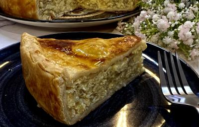 Foto da receita de Torta de Cebola e Ovos. Observa-se um pedaço grande de torta em um prato preto com decoração de flores brancas. Foto da receita de Torta de Cebola e Ovos. Observa-se um pedaço grande de torta em um prato preto com decoração de flores brancas.