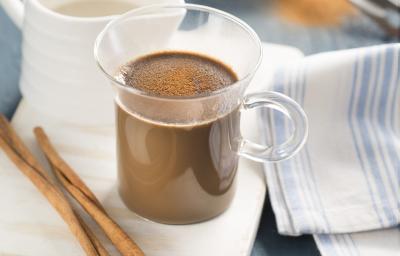 fotografia em tons de branco, marrom e azul tirada de uma xicara transparente com o Cappuccino dentro, e ao lado direito contém uma xicara branca e à frente canela. fotografia em tons de branco, marrom e azul tirada de uma xicara transparente com o Cappuccino dentro, e ao lado direito contém uma xicara branca e à frente canela.