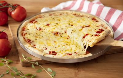 Fotografia em tons de vermelho em uma bancada de madeira clara, uma tábua de madeira, um pano branco com listras vermelhas, uma forma de pizza com a pizza de muçarela em cima dela e uma espátula de madeira tirando um pedaço. Ao lado, tomates para decorar. Fotografia em tons de vermelho em uma bancada de madeira clara, uma tábua de madeira, um pano branco com listras vermelhas, uma forma de pizza com a pizza de muçarela em cima dela e uma espátula de madeira tirando um pedaço. Ao lado, tomates para decorar.