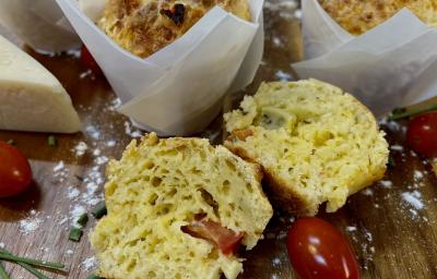 Foto da Receita de Muffin de Pizza. Observa-se um muffin cortado ao meio em cima de uma tábua de madeira. Tomates cereja e queijo decoram a foto também Foto da Receita de Muffin de Pizza. Observa-se um muffin cortado ao meio em cima de uma tábua de madeira. Tomates cereja e queijo decoram a foto também