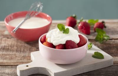 Fotografia em tons de vermelho em uma bancada de madeira clara, uma tábua de madeira branca, um potinho rosa claro com morangos dentro cobertos com creme de leite fresco. Ao fundo, um potinho vermelho com o creme de leite fresco dentro dele. Fotografia em tons de vermelho em uma bancada de madeira clara, uma tábua de madeira branca, um potinho rosa claro com morangos dentro cobertos com creme de leite fresco. Ao fundo, um potinho vermelho com o creme de leite fresco dentro dele.