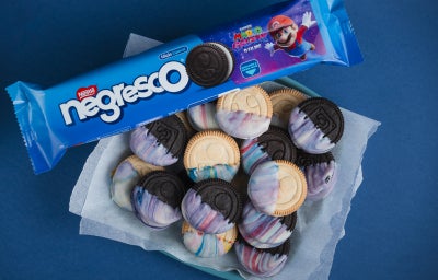 Prato azul com biscoitos decorados com cobertura marmorizada, acompanhado de embalagem Negresco apoiada na borda.