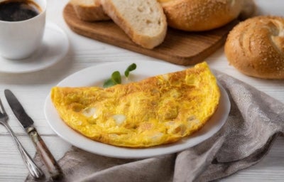 Fotografia mostra Omelete dourada servida dobrada no prato.