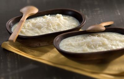 Fotografia em tons de marrom, branco e bege, com dois recipientes de madeira escura com tapioca, coco ralado e duas colheres de pau sobre guardanapo bege, tudo sobre bancada em tons de cinza. Fotografia em tons de marrom, branco e bege, com dois recipientes de madeira escura com tapioca, coco ralado e duas colheres de pau sobre guardanapo bege, tudo sobre bancada em tons de cinza.