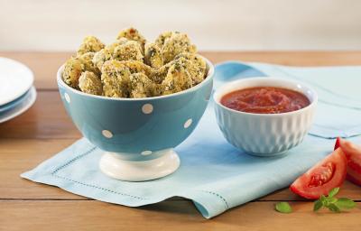 Fotografia em tons de marrom e azul claro de uma mesa de madeira vista de frente, contém um pano cor azul claro e por cima um recipiente redondo cor azul com bolinhas brancas com pedaços de nuggets, ao lado um pote branco com molho de tomate. Fotografia em tons de marrom e azul claro de uma mesa de madeira vista de frente, contém um pano cor azul claro e por cima um recipiente redondo cor azul com bolinhas brancas com pedaços de nuggets, ao lado um pote branco com molho de tomate.