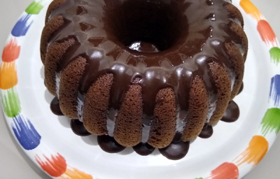 Foto em tons de marrom da receita de bolo de café servida com uma cobertura de chocolate por cima e sobre um prato branco com a borda colorida Foto em tons de marrom da receita de bolo de café servida com uma cobertura de chocolate por cima e sobre um prato branco com a borda colorida