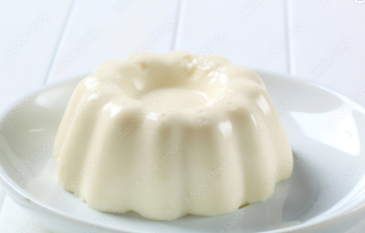 Fotografia de um pudim de leite ninho sobre um prato branco, o qual está apoiado em uma mesa branca.