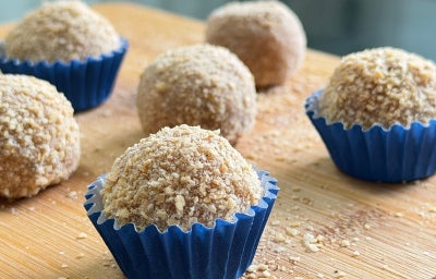Fotografia mostra brigadeiros enrolados em farinha lactea enformados em forminhas de brigadeiro azul.
