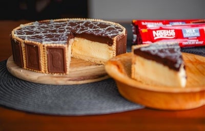 Fotografia de uma torta holandesa com um pedaço grande sobre um prato de madeira pequeno. A torta está em uma tábua redonda de madeira.