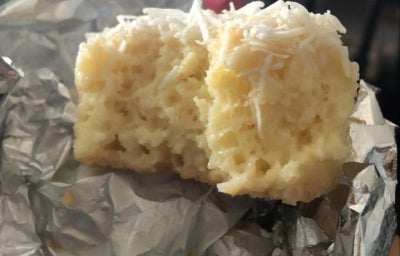 Bolo gelado de coco cortado ao meio, coberto com coco ralado e apoiado sobre papel-alumínio.