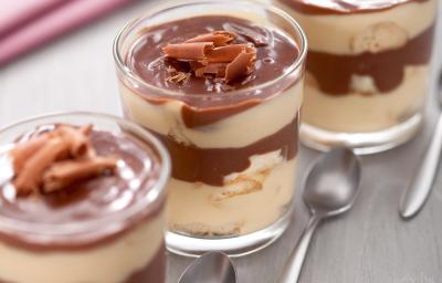 Fotografia em tons de marrom em uma bancada de madeira clara com um pano rosa de fundo e três taças de vidro com pavê de chocolate com maracujá e raspas de chocolate para enfeitar. Fotografia em tons de marrom em uma bancada de madeira clara com um pano rosa de fundo e três taças de vidro com pavê de chocolate com maracujá e raspas de chocolate para enfeitar.