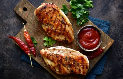 Fotografia de um peito de frango fatiado servido com molho picante.