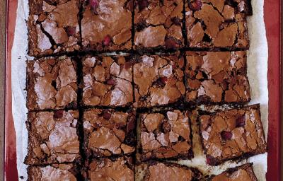 fotografia em tons de marrom e branco de uma bancada vista de cima, contém um pano branco e por cima pedaços quadrados de bolo de chocolate