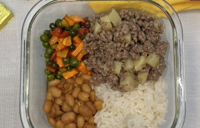 Fotografia em tons de amarelo e vermelho com uma receita de marmita de carne moida com batata acompanhada de arroz, feijão e leguemes.