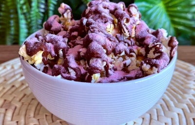 Fotografia em tons de rosa e marrom com um pote branco ao centro. Dentro do prato existe uma receita de pipoca doce coberta com chocolate meio amargo e polvilhada com Nesquik Fotografia em tons de rosa e marrom com um pote branco ao centro. Dentro do prato existe uma receita de pipoca doce coberta com chocolate meio amargo e polvilhada com Nesquik