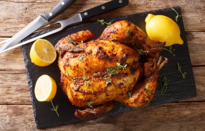 Imagem de uma tábua com um peru assado com ervas, limões ao lado e um garfo e faca.