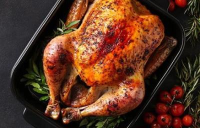 A imagem mostra um frango assado em uma travessa escura com ervas em sua volta A imagem mostra um frango assado em uma travessa escura com ervas em sua volta