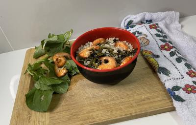 Imagem da receita de Arroz Paraense Nutritivo em um recipiente, sobre uma tábua, e ao lado folhas der jambu e camarão