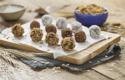 fotografia em tons de azul em uma bancada de madeira clara, uma tábua de madeira, um paninho azul escuro e vários docinhos parecidos com brigadeiros, mas feitos com Nesfit e sem açúcar. Ao fundo, potinhos com Nesfit Cereais. fotografia em tons de azul em uma bancada de madeira clara, uma tábua de madeira, um paninho azul escuro e vários docinhos parecidos com brigadeiros, mas feitos com Nesfit e sem açúcar. Ao fundo, potinhos com Nesfit Cereais.