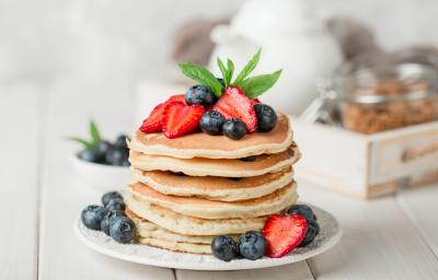Fotografia de uma torre de panquecas e pedaços de frutas.