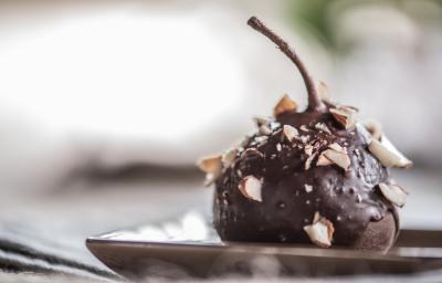Fotografia de uma pera coberta com chocolate à base de Neston e lascas de nozes sobre um prato de vidro de cor clara. Fotografia de uma pera coberta com chocolate à base de Neston e lascas de nozes sobre um prato de vidro de cor clara.