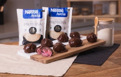 Foto da receita de bites proteicas de frutas vermelhas servidas em diversas porções sobre uma tábua bicolor em cima de uma mesa de madeira com um pote de aveia ao lado Foto da receita de bites proteicas de frutas vermelhas servidas em diversas porções sobre uma tábua bicolor em cima de uma mesa de madeira com um pote de aveia ao lado