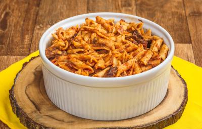 Foto de uma bancada de madeira e bem ao centro há uma toalha amarela, uma tábua de madeira e sobre ela um recipiente redondo e branco. Dentro dele está a receita de macarrão tipo penne com carne desfiada.
