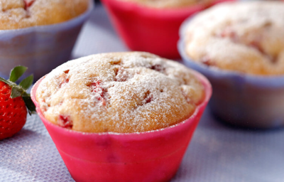 Fotografia em tons de vermelho e lilás em uma bancada com uma toalha emborrachada lilás, com forminhas pequenas vermelhas e lilás com os muffins de fubá com morango dentro delas. Fotografia em tons de vermelho e lilás em uma bancada com uma toalha emborrachada lilás, com forminhas pequenas vermelhas e lilás com os muffins de fubá com morango dentro delas.