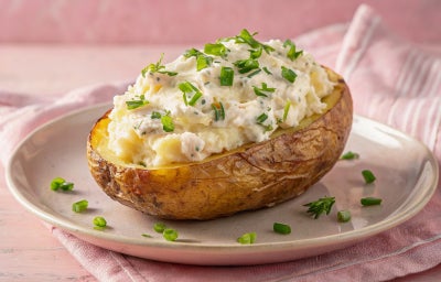 Imagem mostra um prato com uma batata grande cortada ao meio e um creme por cima recheando-a