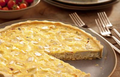 Fotografia em tons de marrom, terrosos e vermelho, com prato em tom terroso contendo uma quiche fatiada e em seu entorno três garfos, pratos empilhados com um pedaço de quiche, potinho com tomate-cereja, tudo sobre bancada de madeira. Fotografia em tons de marrom, terrosos e vermelho, com prato em tom terroso contendo uma quiche fatiada e em seu entorno três garfos, pratos empilhados com um pedaço de quiche, potinho com tomate-cereja, tudo sobre bancada de madeira.