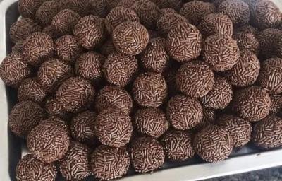 Fotografia de vários brigadeiros de café passados no granulado tradicional. Os brigadeiros estão dentro de uma forma grande retangular de alumínio.