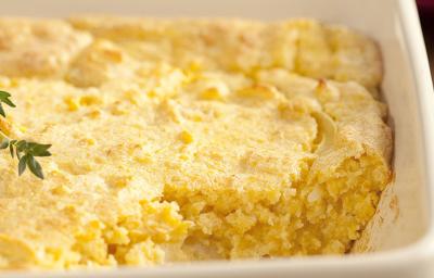 Fotografia em tons de branco e amarelo de uma bancada de madeira com um recipiente retangular branco com a sopa paraguaia.