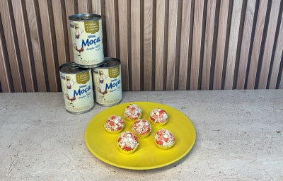 Prato amarelo com docinhos decorados com confeitos de coração vermelhos e brancos, com Leite Moça ao fundo.
