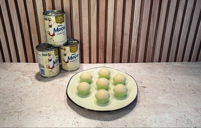 Fotografia em tons de bege, em uma bancada, Leite Moça ao fundo e prato com brigadeiros ao centro.