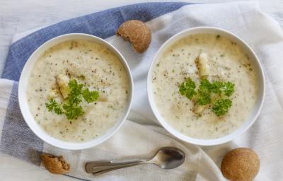 Fotografia vista de cima de dois recipientes na cor branca com um creme de aveias com palmito, pimenta por cima e salsinha. Ao redor, três biscoitos e uma colher de sopa, sobre uma toalha de mesa branca com faixas em azul. Fotografia vista de cima de dois recipientes na cor branca com um creme de aveias com palmito, pimenta por cima e salsinha. Ao redor, três biscoitos e uma colher de sopa, sobre uma toalha de mesa branca com faixas em azul.