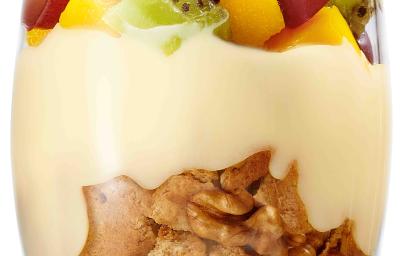 fotografia tirada de um copo transparente com biscoitos triturados, leite MOÇA e frutas por cima.